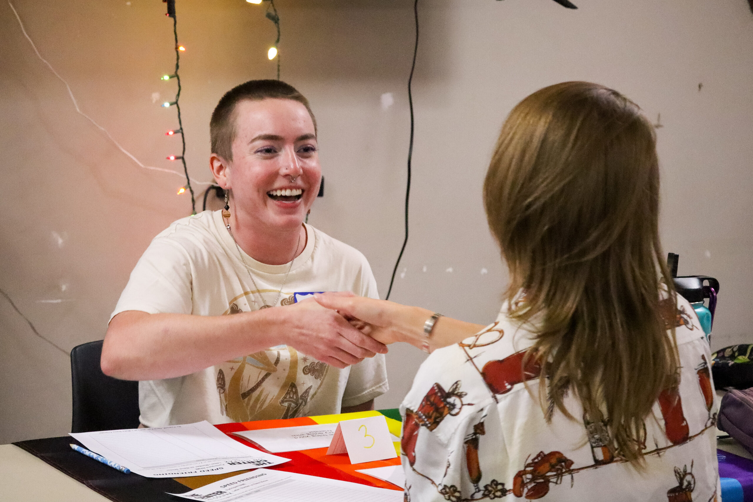 Two people facing each other, shaking hands. One person has a big smile and other person's back is observed.
