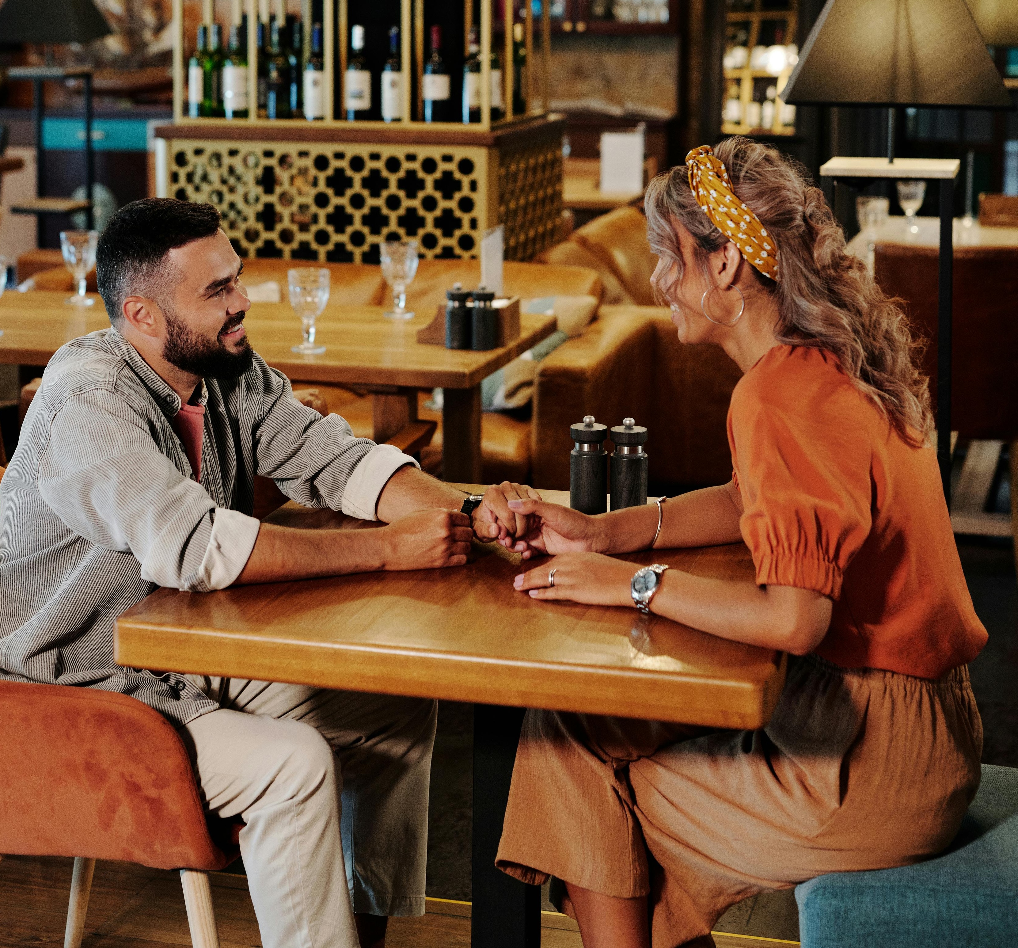Two people sit opposite each other at a small table. They are making eye contact and their hands are touching.